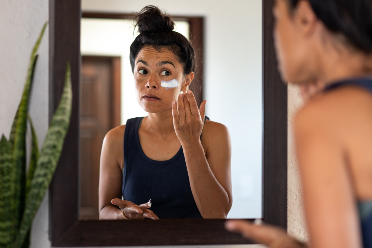 a woman putting on sun screen in front of a mirror in a room